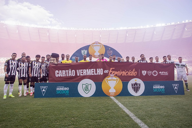 Atletas do América e Atlético seguram faixa na final do Campeonato Mineiro. A faixa é vemelha e tem escrito Cartão Vermelho ao Feminicídio